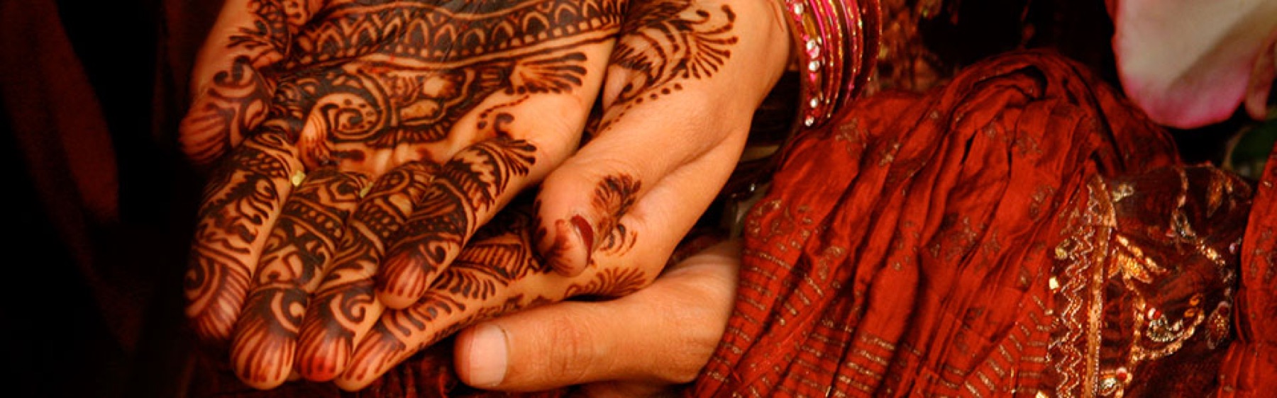 Henna patterns drawn across a pair of open hands, a red and gold sari beside them
