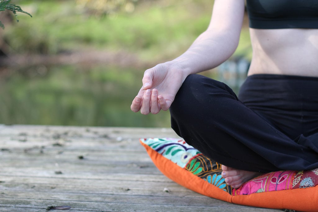 A woman meditating cross-legged on a jetty by the water