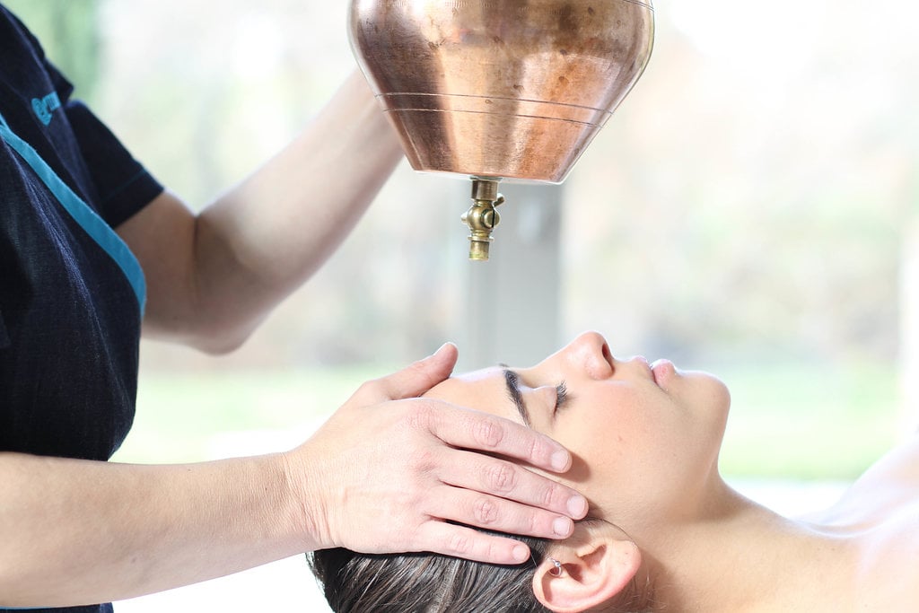 Shirodhara, warm oil poured from a copper vessel onto a guest's forehead