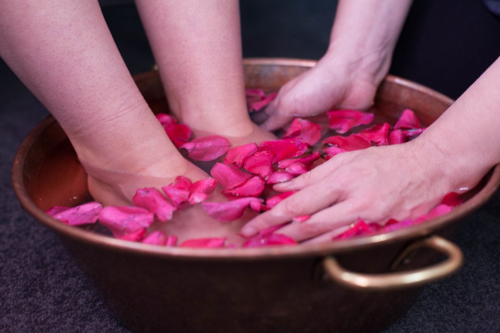 Hands in a copper bowl of rose petals, the foot bath that opens every treatment