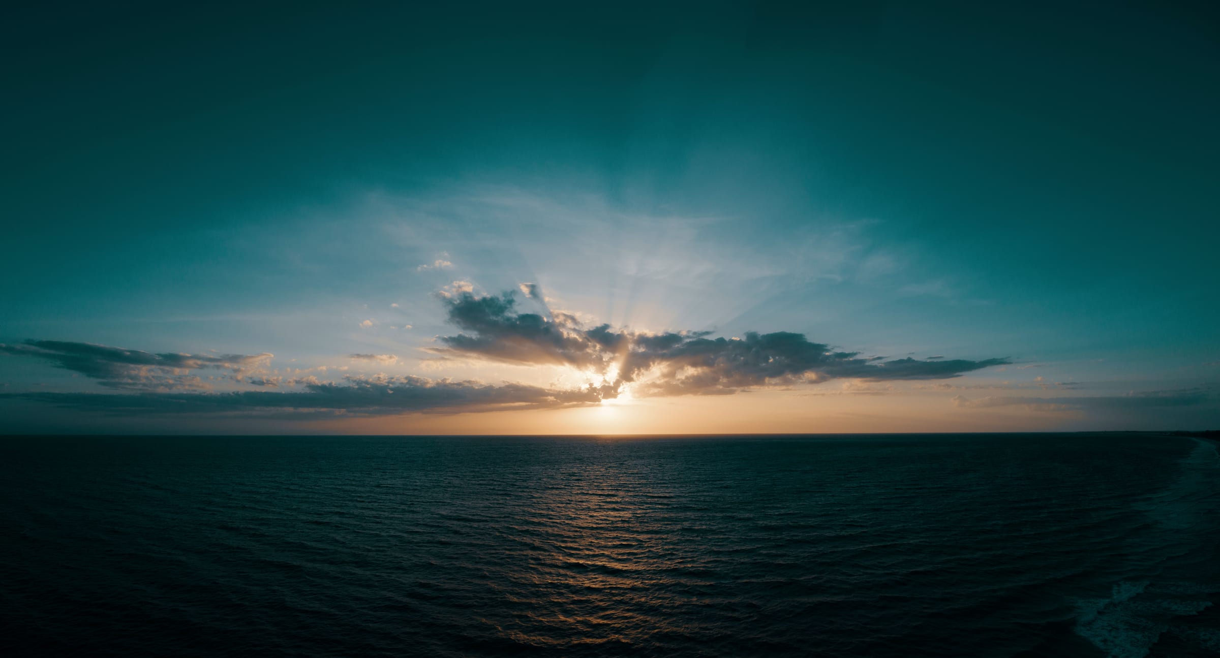 The sun breaking through cloud over a teal sea