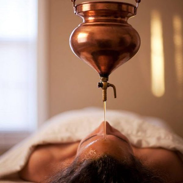 Warm oil streaming onto a guest's forehead during shirodhara