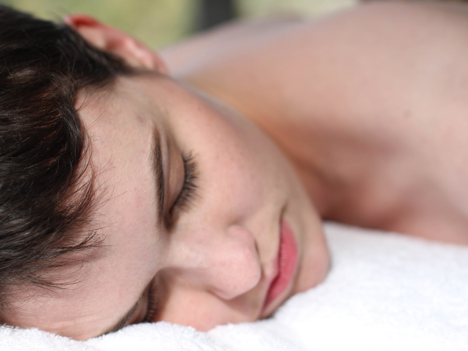 A woman resting her head on a white towel on the massage table, eyes closed