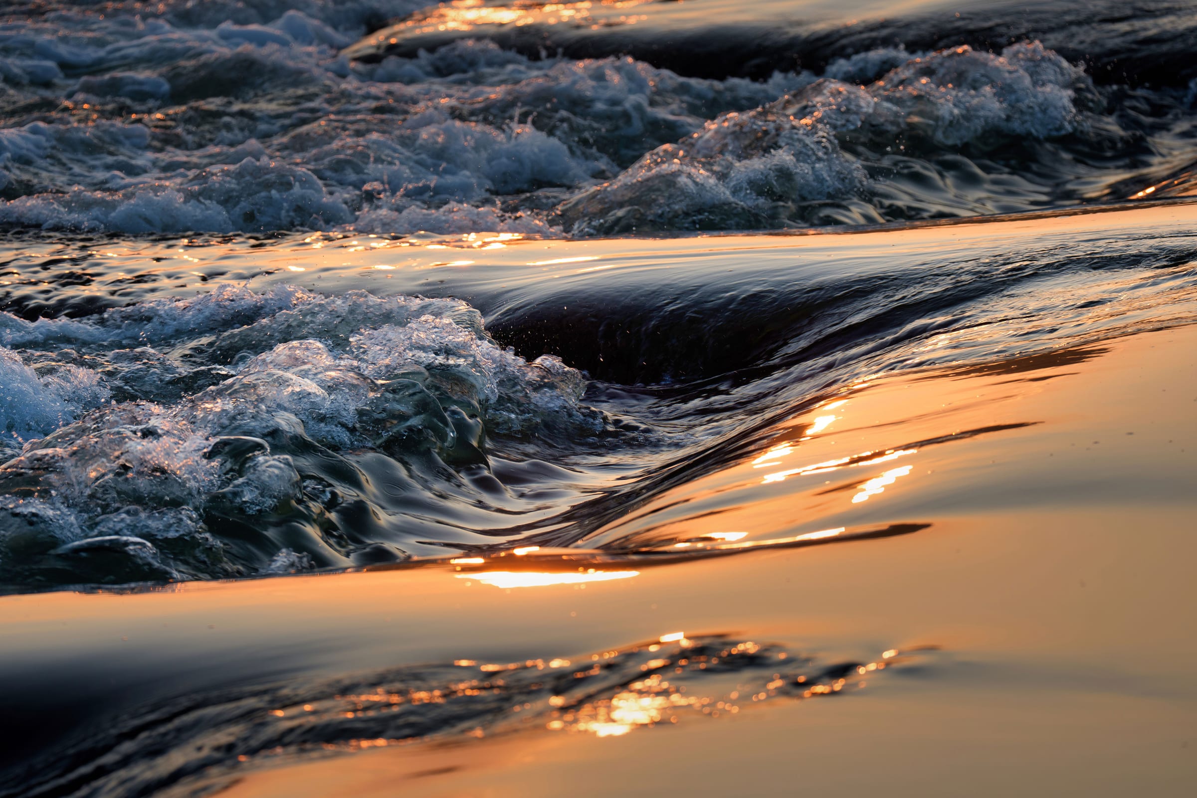 Waves washing over sand at sunset